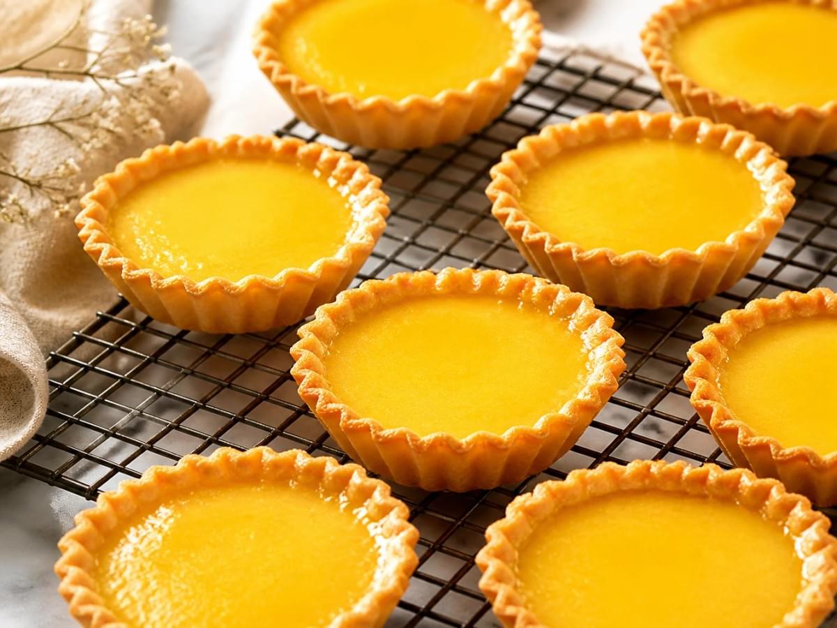 Golden egg tarts resting on a black wire cooling rack. Golden egg tarts resting on a black wire cooling rack.
