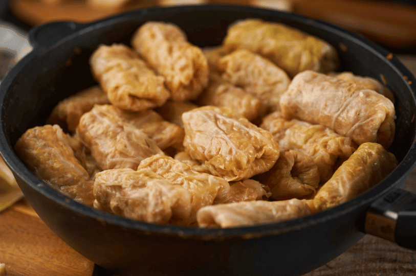 A close-up side angle of plump, freshly cooked Romanian stuffed cabbage rolls resting in a dark skillet. A close-up side angle of plump, freshly cooked Romanian stuffed cabbage rolls resting in a dark skillet.