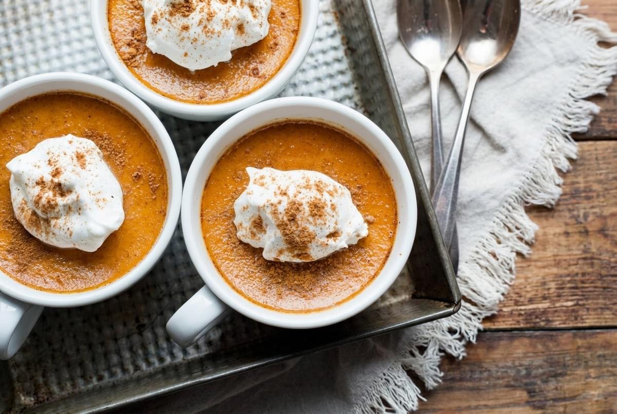Small white ramekins filled with pumpkin pudding topped with whipped cream and ground cinnamon. Small white ramekins filled with pumpkin pudding topped with whipped cream and ground cinnamon.