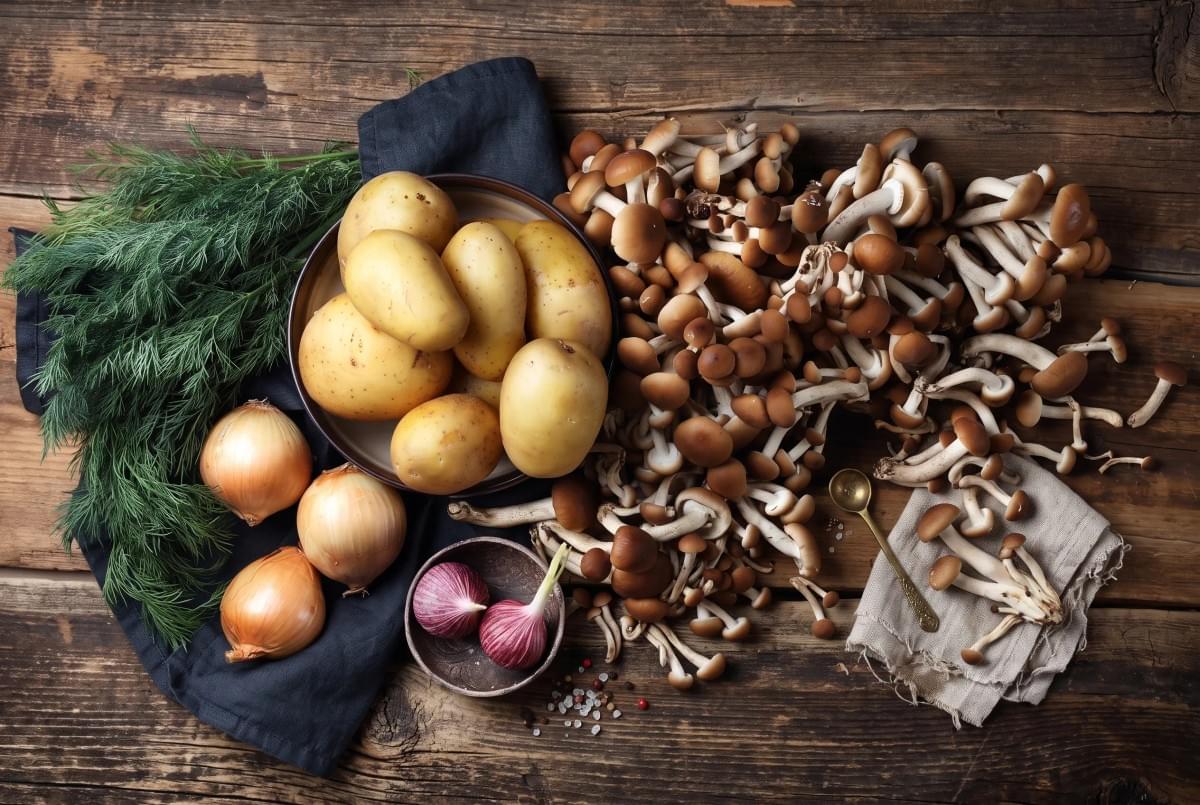 Flat lay display of raw potatoes, brown mushrooms, onions, and fresh dill on a rustic wooden surface. Flat lay display of raw potatoes, brown mushrooms, onions, and fresh dill on a rustic wooden surface.