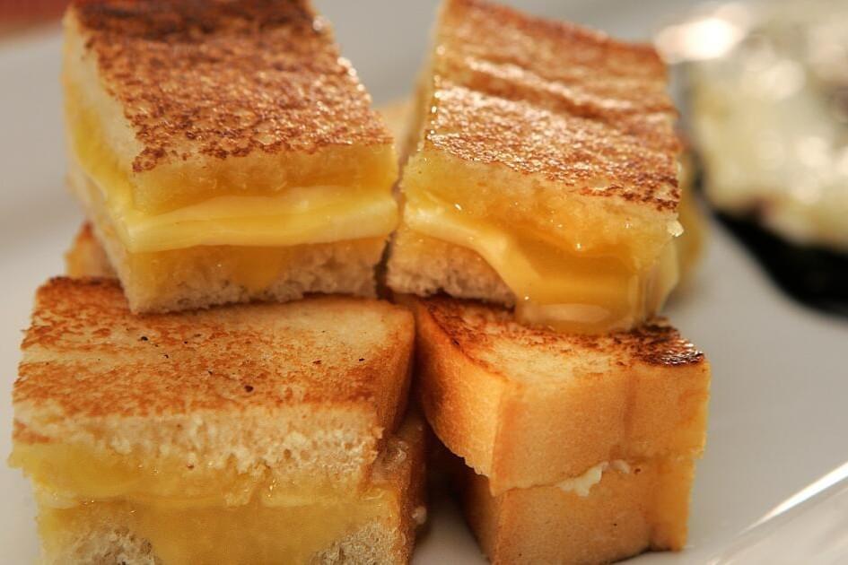 The image shows four small, rectangular grilled cheese sandwiches stacked neatly on top of each other. The bread is perfectly golden-brown and toasted, with warm, melted cheese oozing out from the centers. The image shows four small, rectangular grilled cheese sandwiches stacked neatly on top of each other. The bread is perfectly golden-brown and toasted, with warm, melted cheese oozing out from the centers.