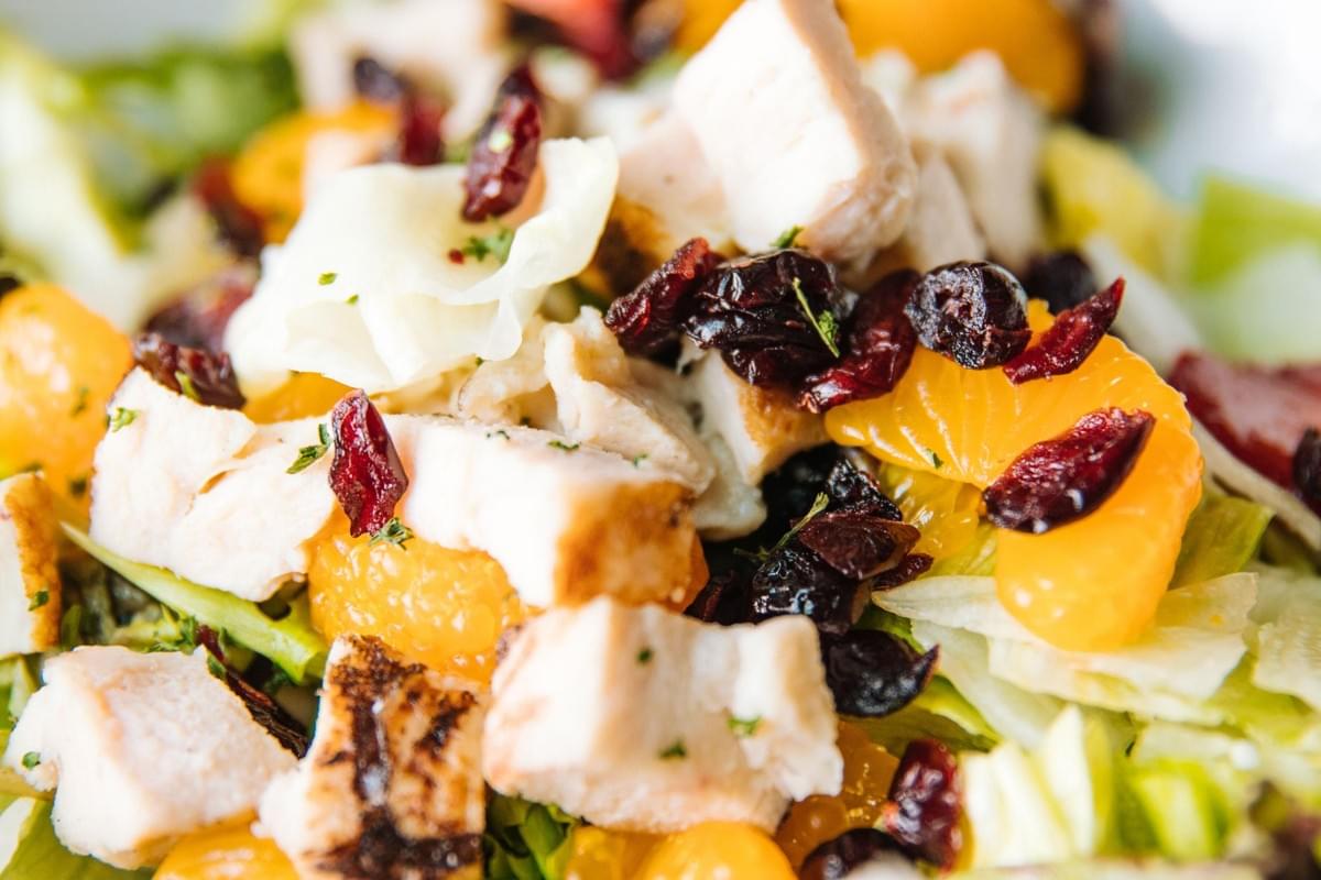 A close-up view of the vibrant salad features diced grilled chicken breast tossed with bright mandarin orange slices. The dish is layered over a bed of crisp green lettuce and garnished with sweet dried cranberries and a sprinkle of fresh herbs. A close-up view of the vibrant salad features diced grilled chicken breast tossed with bright mandarin orange slices. The dish is layered over a bed of crisp green lettuce and garnished with sweet dried cranberries and a sprinkle of fresh herbs.