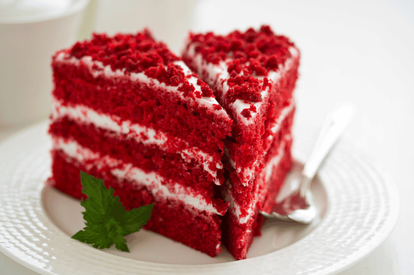Two slices of beautifully colored red velvet cake on a textured white plate, garnished with a sprig of mint to emphasize the striking, vibrant red hue and soft crumb. Two slices of beautifully colored red velvet cake on a textured white plate, garnished with a sprig of mint to emphasize the striking, vibrant red hue and soft crumb.