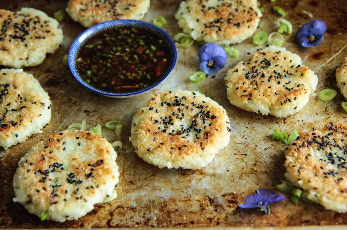 A serving tray of golden crispy rice cakes with a side of flavorful dipping sauce. A serving tray of golden crispy rice cakes with a side of flavorful dipping sauce.