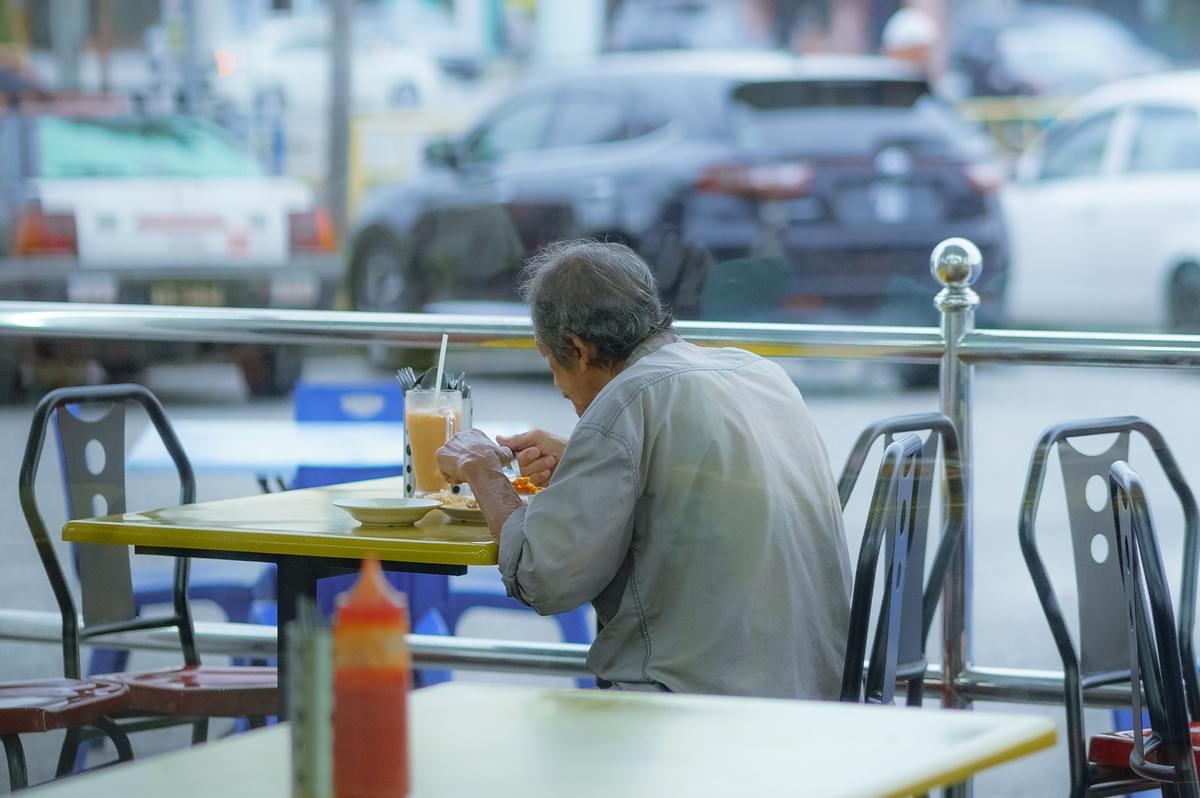 An elderly person eating a quiet meal alone at a table near a window. An elderly person eating a quiet meal alone at a table near a window.