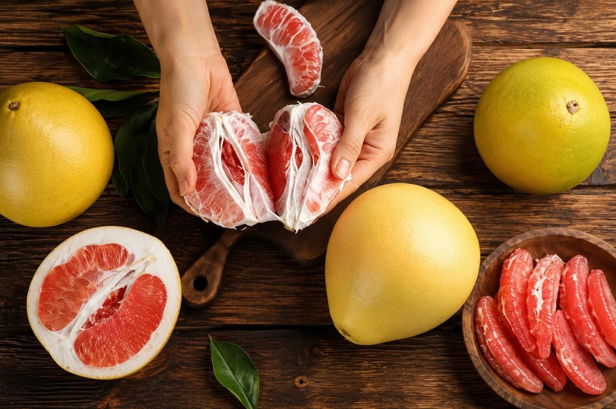 Hands peeling open a pink pomelo on a wooden table surrounded by whole and sliced pomelos. Hands peeling open a pink pomelo on a wooden table surrounded by whole and sliced pomelos.
