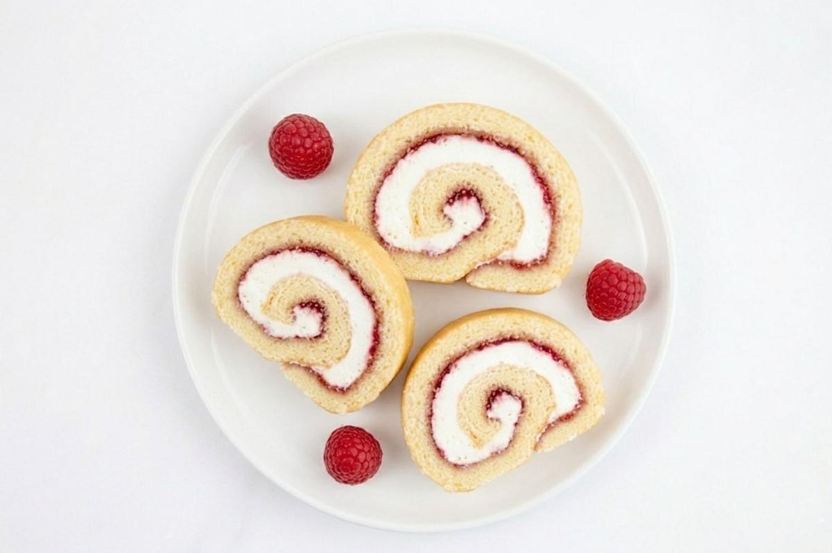 Three slices of Swiss roll cake with cream and raspberry filling on a white plate with fresh raspberries Three slices of Swiss roll cake with cream and raspberry filling on a white plate with fresh raspberries
