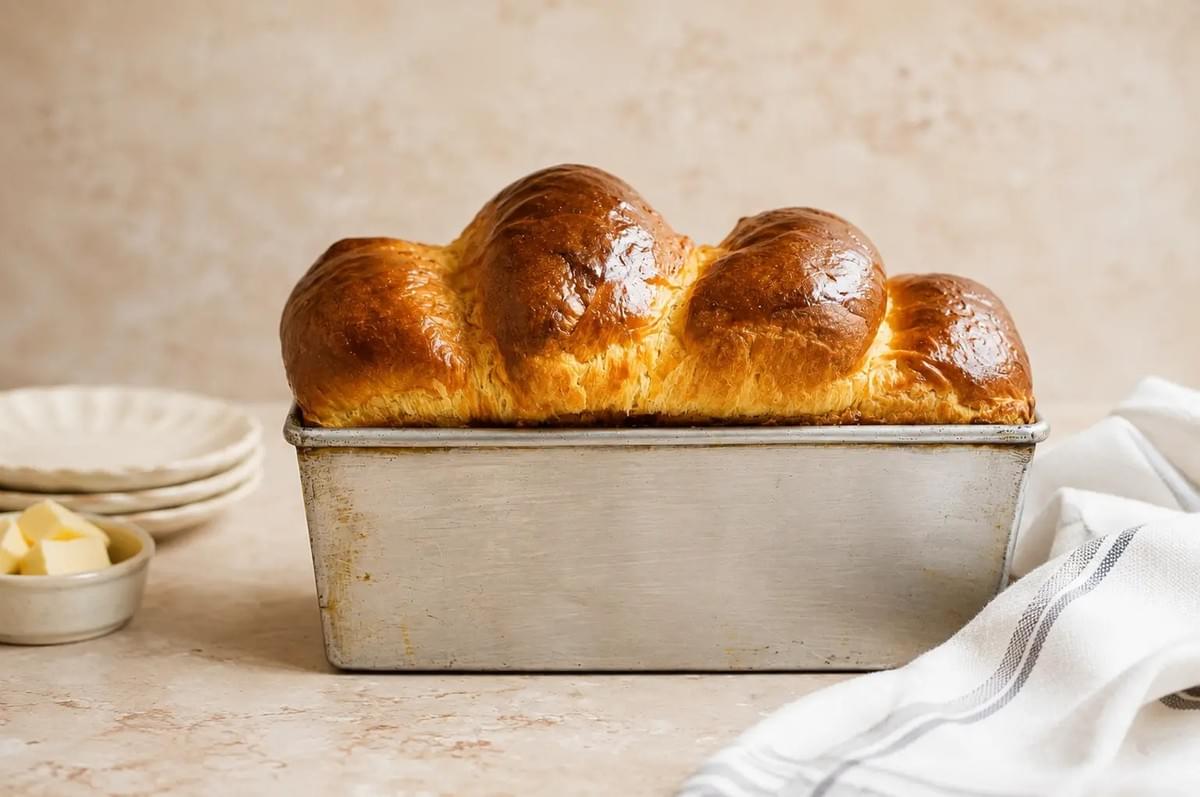 Freshly baked brioche loaf with golden domed tops sitting in a metallic baking pan. Freshly baked brioche loaf with golden domed tops sitting in a metallic baking pan.