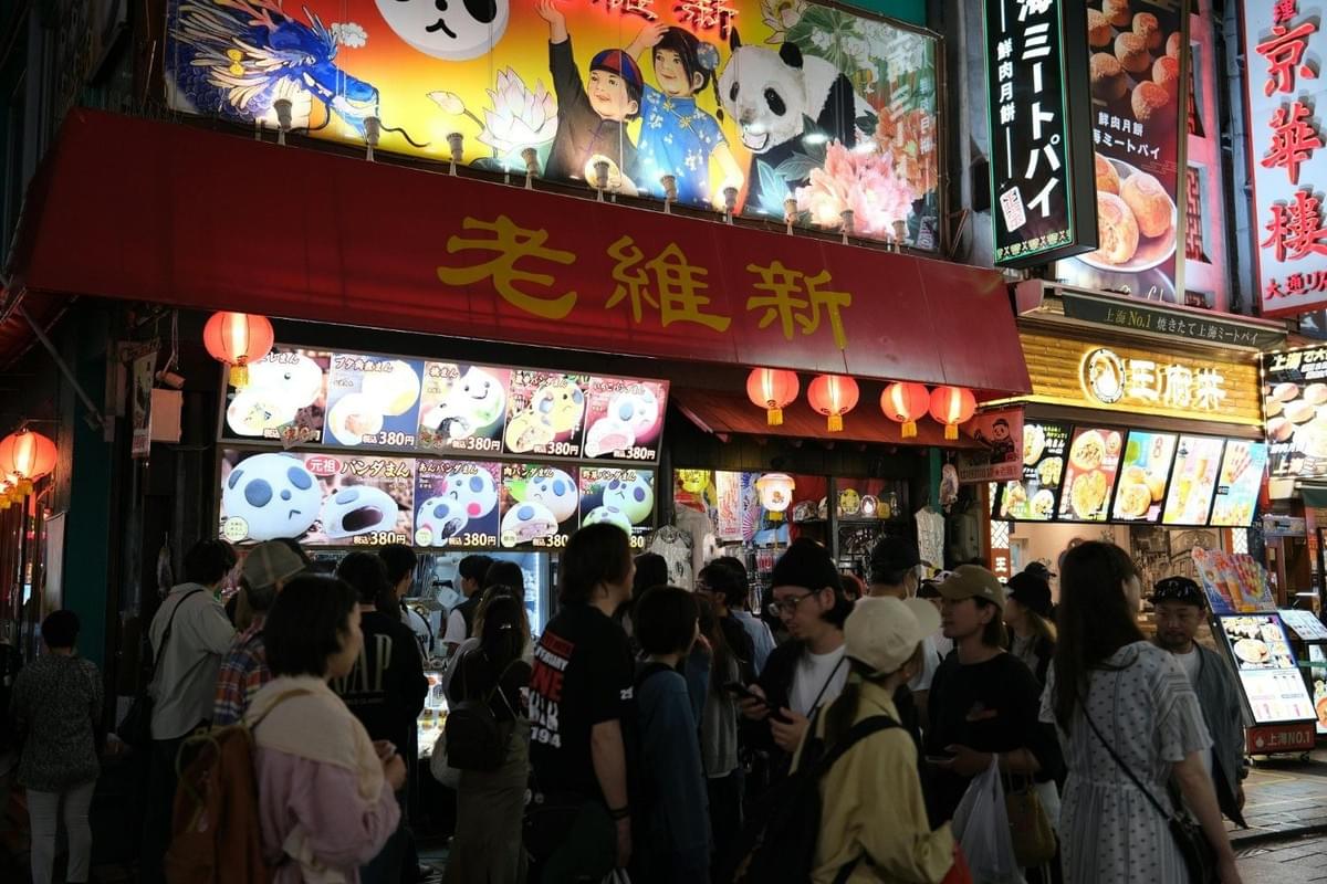 Vibrant nighttime street scene at a busy Asian food district, showcasing colorful neon signs and people queuing for late-night makan (food). Vibrant nighttime street scene at a busy Asian food district, showcasing colorful neon signs and people queuing for late-night makan (food).