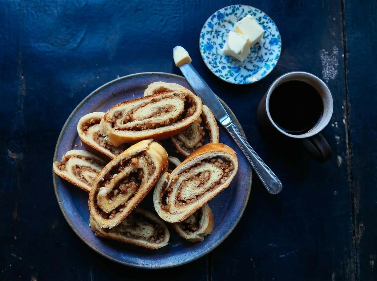 Deep golden crust heavily dusted with snowy white powdered sugar, rich cinnamon-brown spirals, and a striking red-and-white gingham apron. Warm, festive, and nostalgic. The action shot of slicing the bread on a rustic wooden table brings a lively, celebratory energy—it feels like a cherished family tradition being shared. Deep golden crust heavily dusted with snowy white powdered sugar, rich cinnamon-brown spirals, and a striking red-and-white gingham apron. Warm, festive, and nostalgic. The action shot of slicing the bread on a rustic wooden table brings a lively, celebratory energy—it feels like a cherished family tradition being shared.
