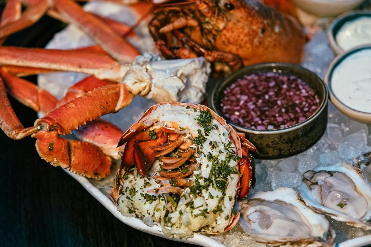 Fresh chilled seafood platter featuring lobster tail with herbs, snow crab legs, and raw oysters served on a bed of ice with dipping sauces. Fresh chilled seafood platter featuring lobster tail with herbs, snow crab legs, and raw oysters served on a bed of ice with dipping sauces.