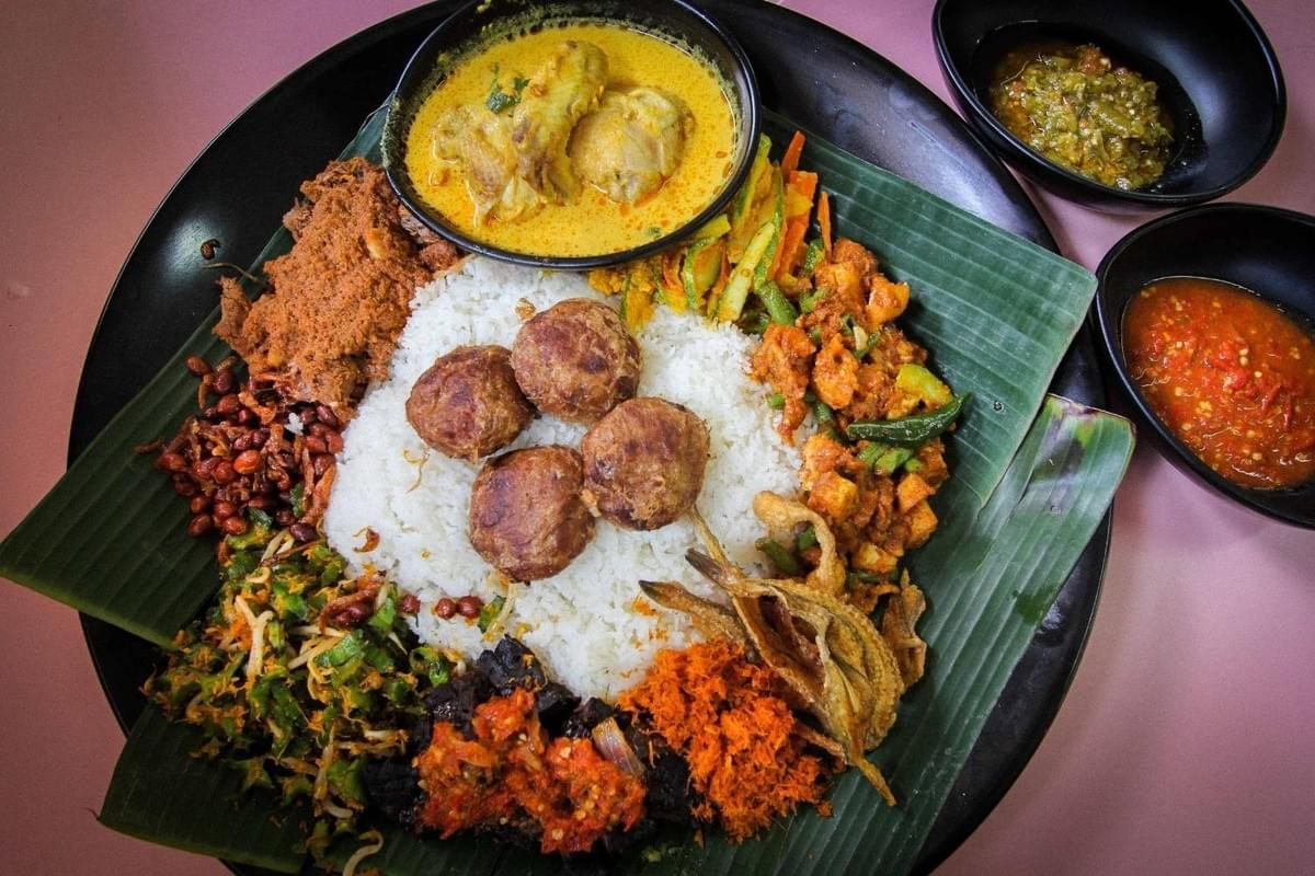 This image showcases a vibrant Nasi Ambeng platter, featuring a central mound of white rice topped with four golden-brown bergedil and surrounded by diverse side dishes like beef rendang, sambal goreng, and fried salted fish. The assortment is presented on a traditional banana leaf and includes bowls of creamy chicken curry along with red and green sambal for extra heat. This image showcases a vibrant Nasi Ambeng platter, featuring a central mound of white rice topped with four golden-brown bergedil and surrounded by diverse side dishes like beef rendang, sambal goreng, and fried salted fish. The assortment is presented on a traditional banana leaf and includes bowls of creamy chicken curry along with red and green sambal for extra heat.