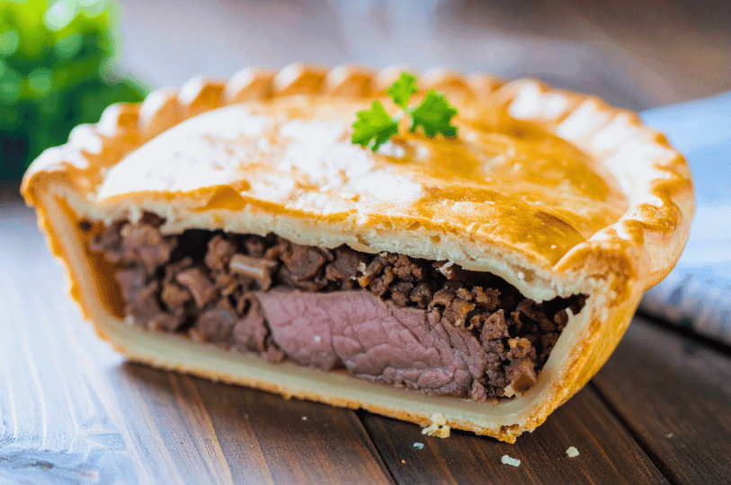 A gourmet Australian meat pie cut in half to reveal a hearty filling of minced meat and a tender subterranean chunk of steak, garnished with parsley. A gourmet Australian meat pie cut in half to reveal a hearty filling of minced meat and a tender subterranean chunk of steak, garnished with parsley.