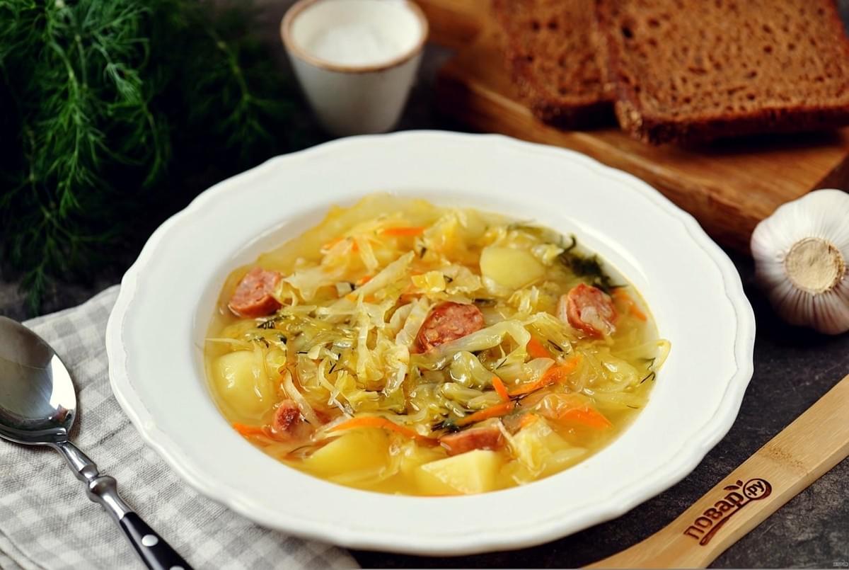 White bowl of savory cabbage and sausage soup served with dark rye bread and garlic. White bowl of savory cabbage and sausage soup served with dark rye bread and garlic.