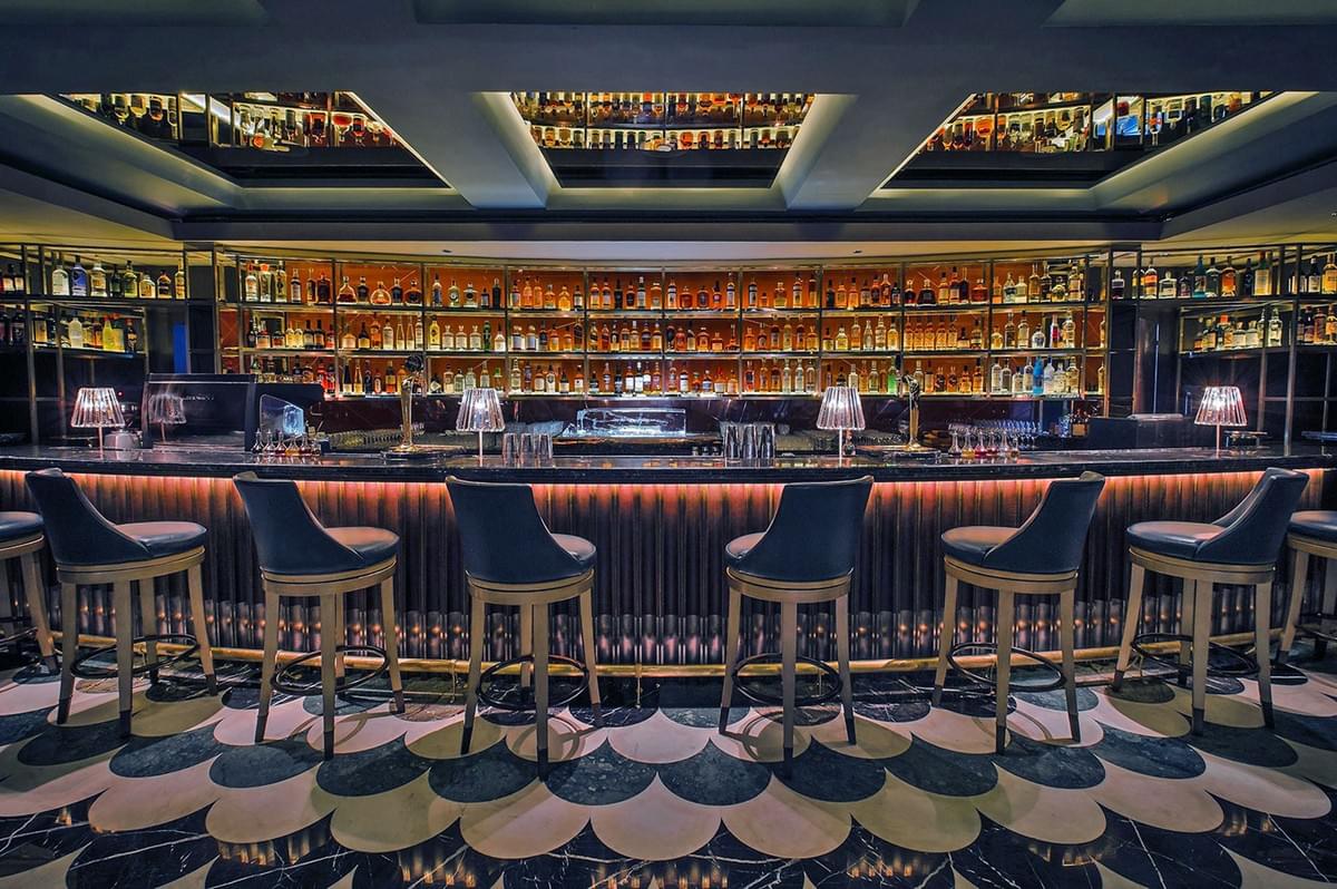 Stylish, dimly-lit bar with a curved marble counter, lined with stools. Bottles are beautifully arranged on shelves, creating an elegant, inviting ambiance. Stylish, dimly-lit bar with a curved marble counter, lined with stools. Bottles are beautifully arranged on shelves, creating an elegant, inviting ambiance.