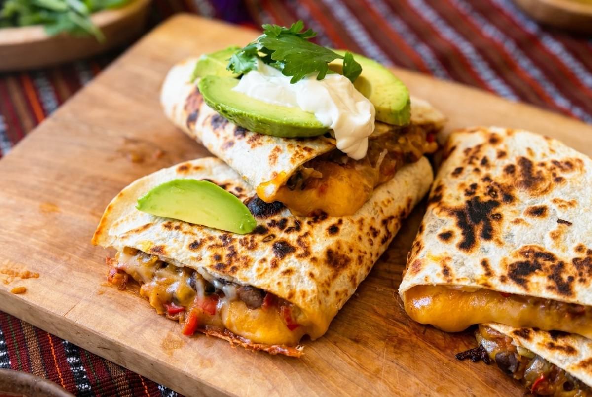 Crispy folded quesadilla filled with melted cheese, black beans, avocado slices, and sour cream. Crispy folded quesadilla filled with melted cheese, black beans, avocado slices, and sour cream.