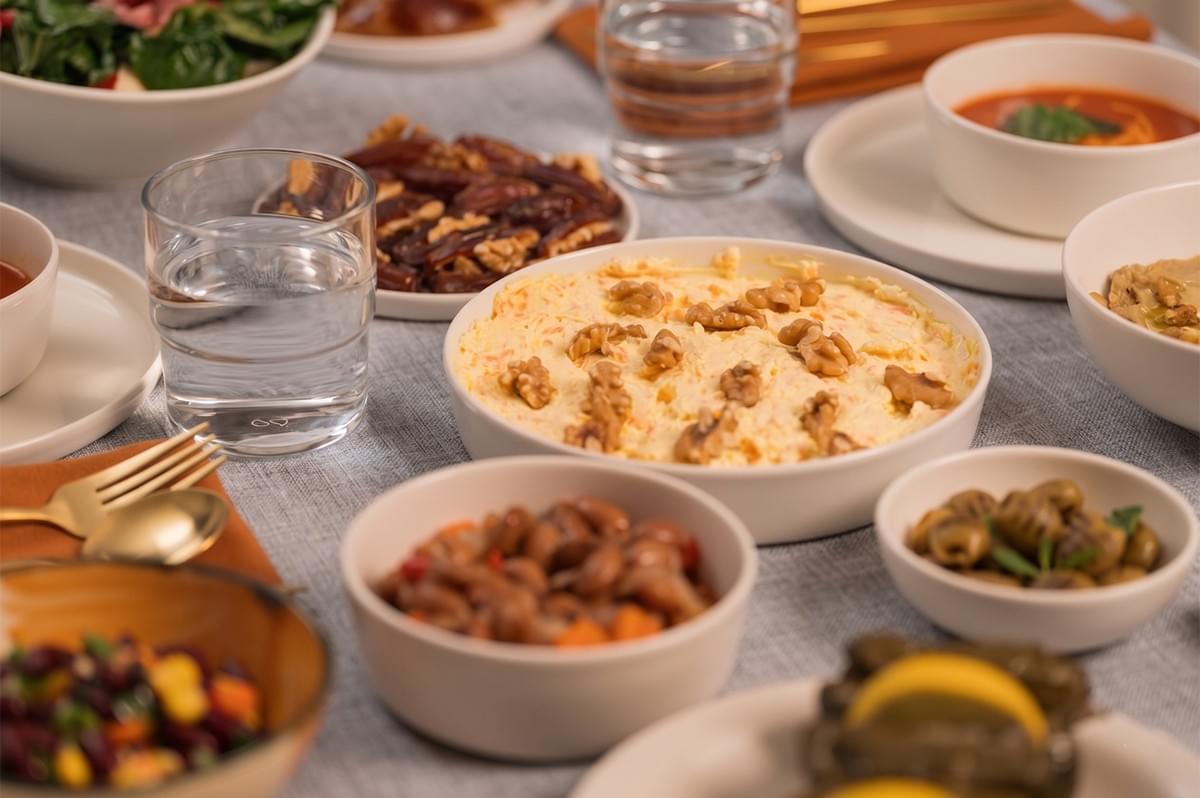 A variety of Middle Eastern appetizers including hummus topped with walnuts, dates, olives, and stuffed grape leaves served on a dining table. A variety of Middle Eastern appetizers including hummus topped with walnuts, dates, olives, and stuffed grape leaves served on a dining table.