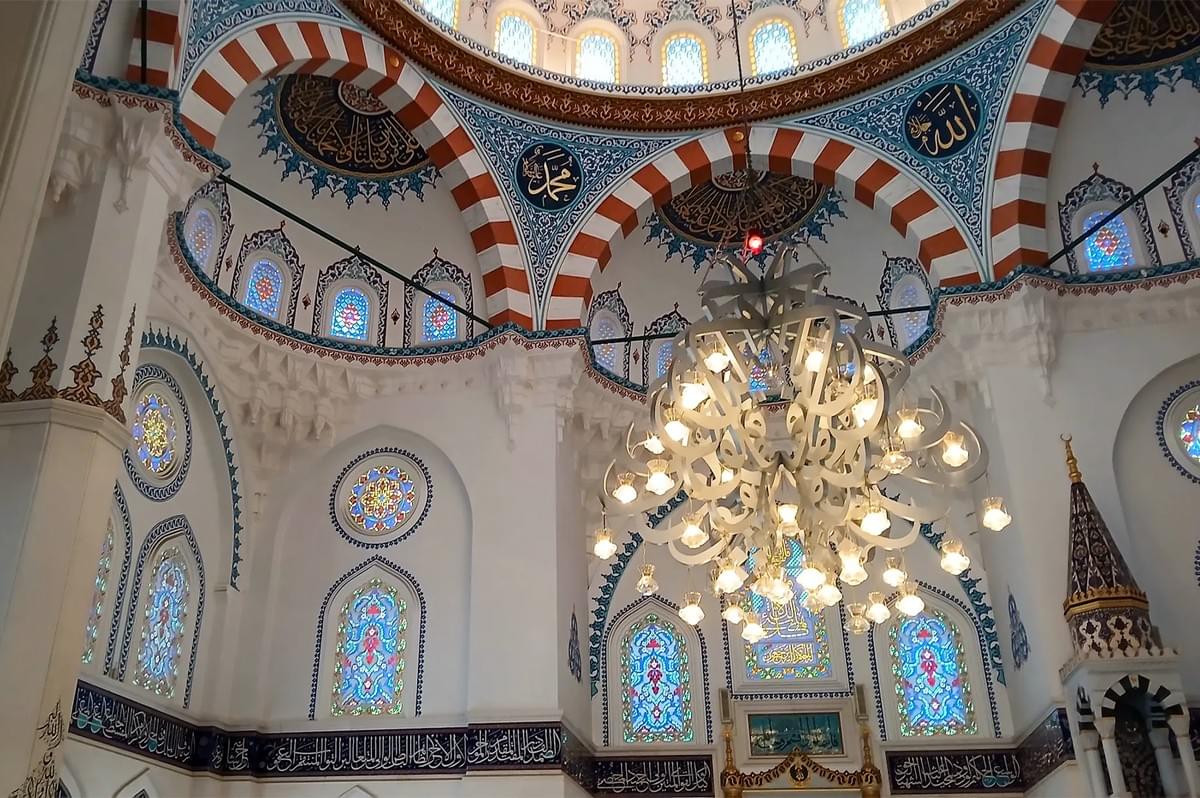 Interior view of a mosque featuring ornate Islamic architecture, intricate stained glass windows, and a large decorative chandelier under a domed ceiling. Interior view of a mosque featuring ornate Islamic architecture, intricate stained glass windows, and a large decorative chandelier under a domed ceiling.