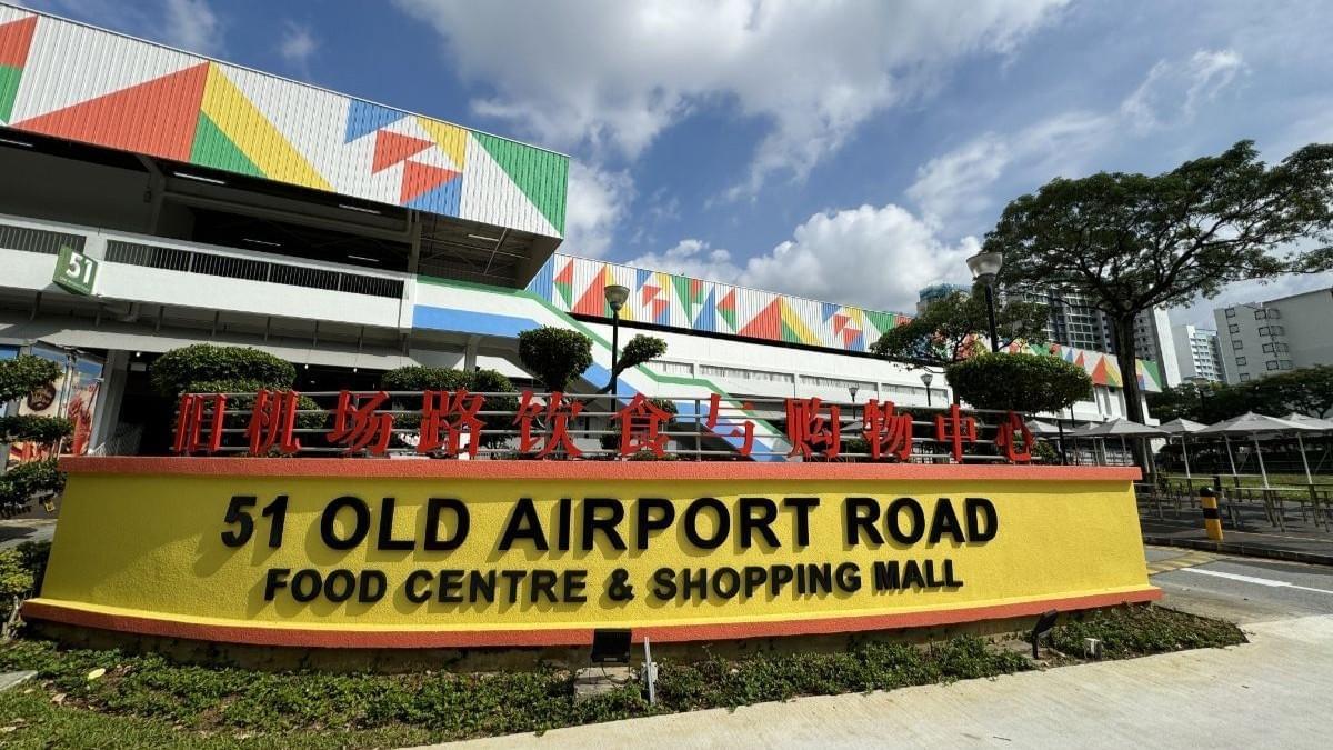 The image features the yellow entrance sign of the 51 Old Airport Road Food Centre & Shopping Mall, set against a backdrop of a colorful, multi-story building and a bright sky. The image features the yellow entrance sign of the 51 Old Airport Road Food Centre & Shopping Mall, set against a backdrop of a colorful, multi-story building and a bright sky.