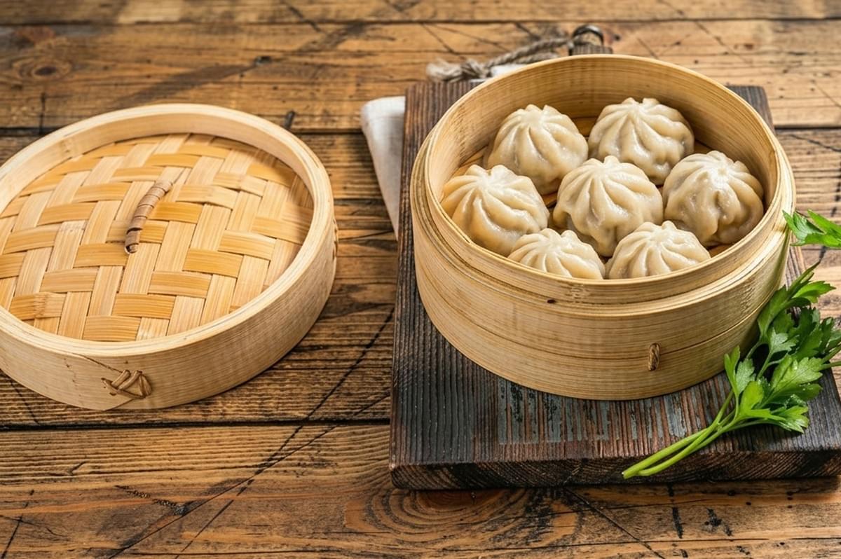 Bamboo steamer filled with cooked Mongolian buuz dumplings on a rustic wooden table with fresh parsley garnish Bamboo steamer filled with cooked Mongolian buuz dumplings on a rustic wooden table with fresh parsley garnish