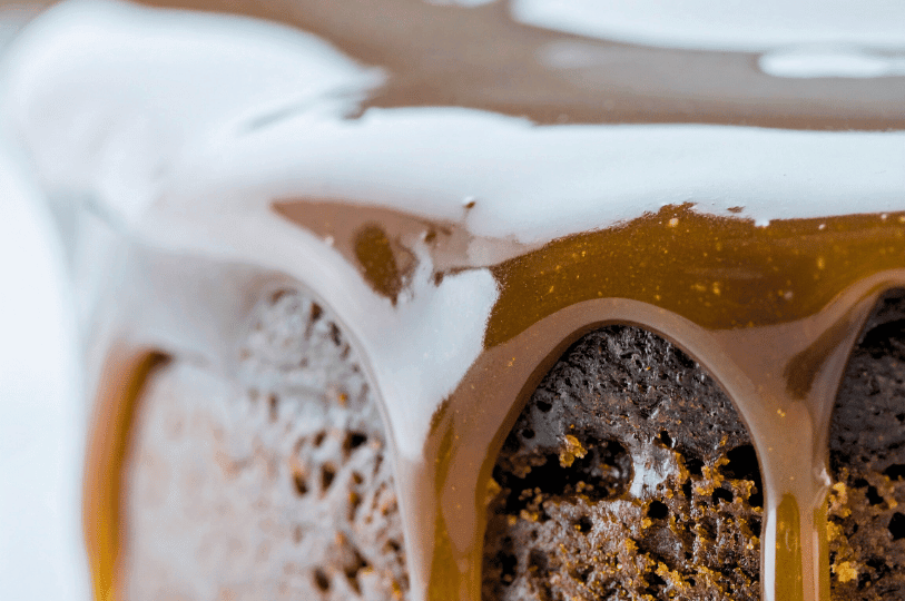 An extreme close-up showing thick, glossy toffee sauce dripping down the sides of a dark pudding. An extreme close-up showing thick, glossy toffee sauce dripping down the sides of a dark pudding.