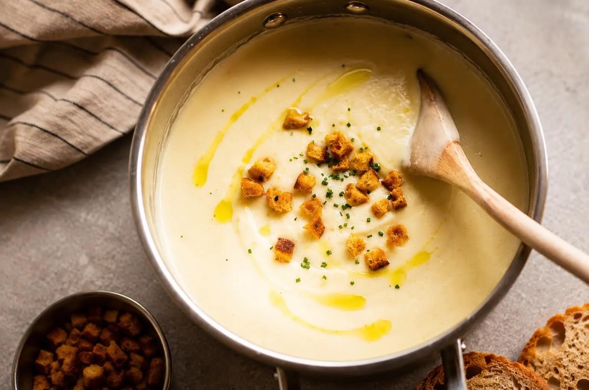 Stainless steel pot filled with creamy celeriac soup, drizzled with olive oil and topped with croutons. Stainless steel pot filled with creamy celeriac soup, drizzled with olive oil and topped with croutons.