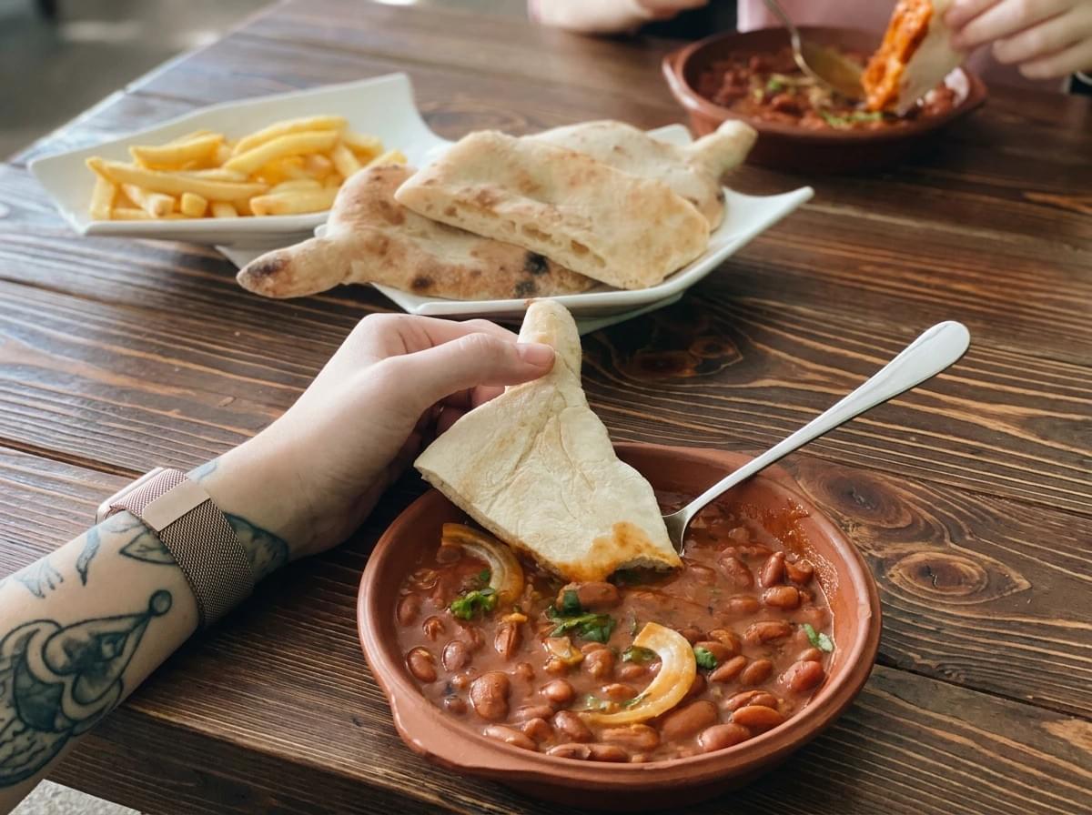 Hand dipping flatbread into a clay dish of spiced red bean stew on a wooden table. Hand dipping flatbread into a clay dish of spiced red bean stew on a wooden table.
