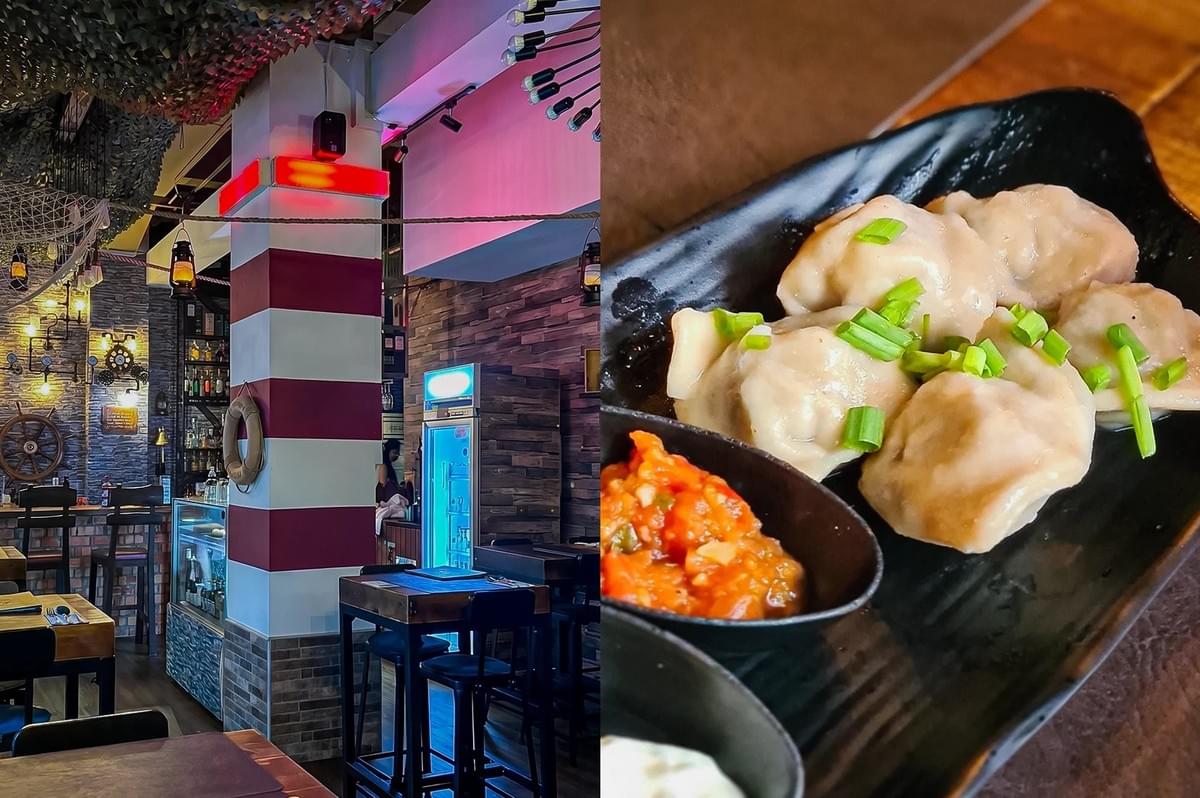 Left: An eye-level, wide-angle interior view of a nautically themed restaurant with eclectic decorations, showcasing a red-and-white striped support pillar holding a lifebuoy, high-top wooden tables with black barstools, brick accent walls, exposed lightbulb fixtures, and a bright beverage cooler under neon pink and blue lighting. Right: A close-up, three-quarter angle culinary shot of several plump, steamed dumplings garnished with freshly chopped green scallions served on a matte black textured plate, accompanied by a small black side dish containing a red chili condiment or salsa. Left: An eye-level, wide-angle interior view of a nautically themed restaurant with eclectic decorations, showcasing a red-and-white striped support pillar holding a lifebuoy, high-top wooden tables with black barstools, brick accent walls, exposed lightbulb fixtures, and a bright beverage cooler under neon pink and blue lighting. Right: A close-up, three-quarter angle culinary shot of several plump, steamed dumplings garnished with freshly chopped green scallions served on a matte black textured plate, accompanied by a small black side dish containing a red chili condiment or salsa.