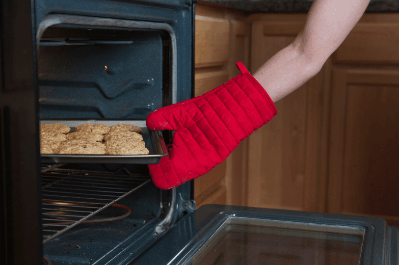 A person wearing a bright red oven mitt removes a tray of freshly baked, golden-brown oatmeal cookies from a hot oven, illustrating the critical timing and temperature awareness needed to prevent overbaking and achieve the perfect chewy texture. A person wearing a bright red oven mitt removes a tray of freshly baked, golden-brown oatmeal cookies from a hot oven, illustrating the critical timing and temperature awareness needed to prevent overbaking and achieve the perfect chewy texture.