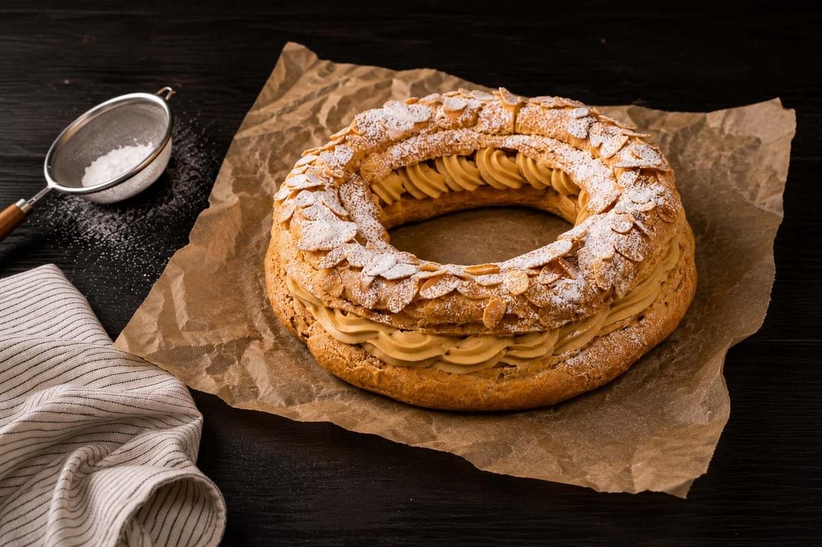 Completed Paris-Brest ring dusted with powdered sugar and topped with sliced almonds on parchment paper Completed Paris-Brest ring dusted with powdered sugar and topped with sliced almonds on parchment paper