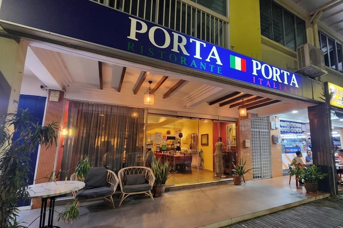 The storefront of Porta Porta Ristorante Italiano, featuring an inviting entrance with cozy outdoor seating, glass doors, and warm interior lighting. The storefront of Porta Porta Ristorante Italiano, featuring an inviting entrance with cozy outdoor seating, glass doors, and warm interior lighting.