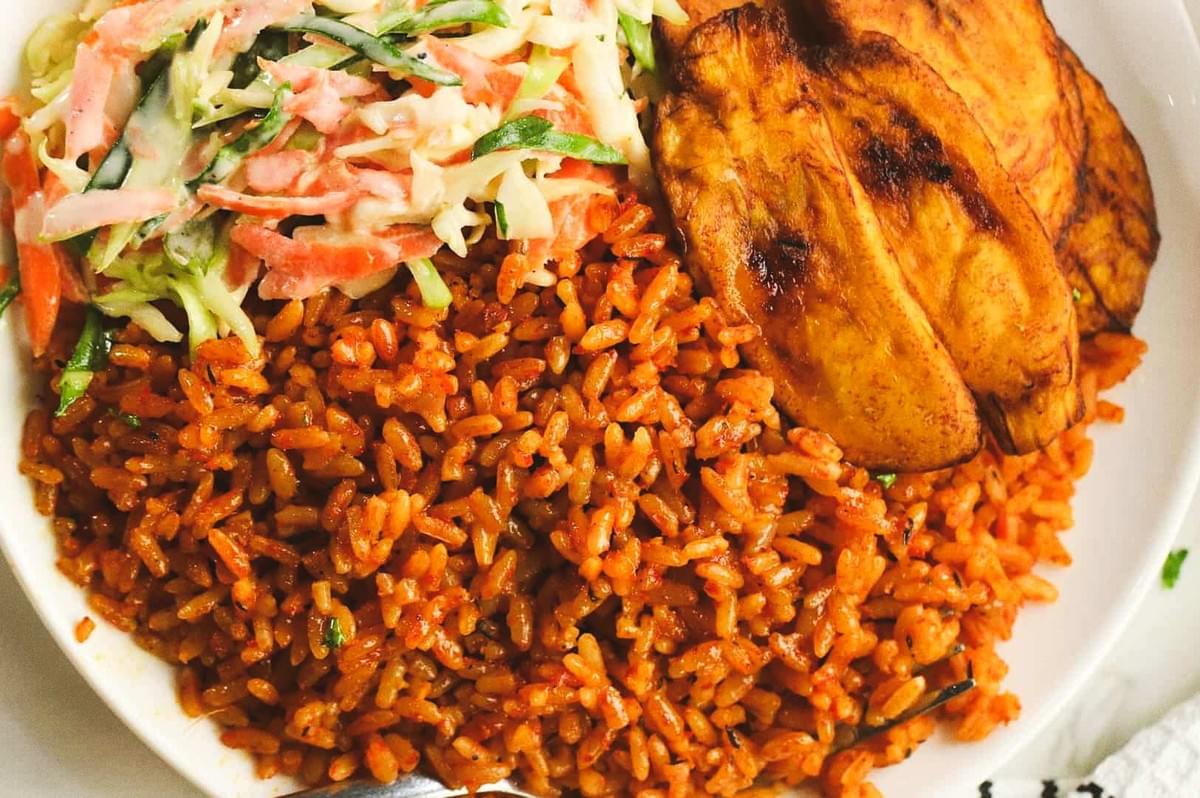 Plate of jollof rice with fried plantains and coleslaw. Plate of jollof rice with fried plantains and coleslaw.