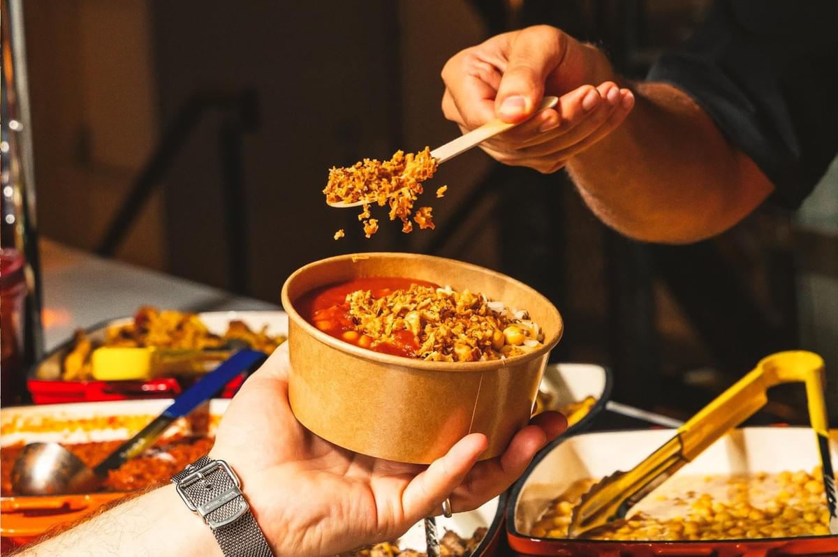 A warm bowl of Egyptian koshari being handed over at a food stall, featuring chickpeas, tomato sauce, and crunchy fried onions. A warm bowl of Egyptian koshari being handed over at a food stall, featuring chickpeas, tomato sauce, and crunchy fried onions.