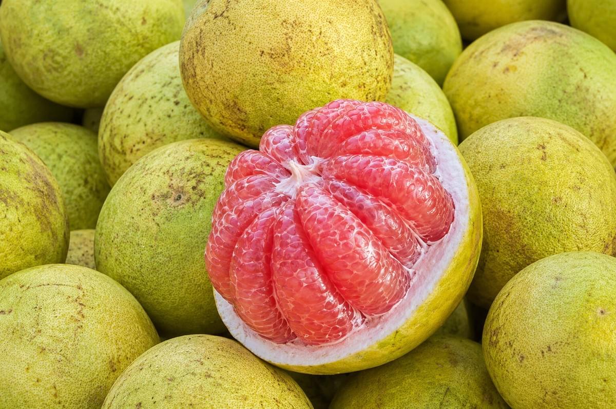 A cut-open pink pomelo resting on a pile of whole, green-yellow pomelos. A cut-open pink pomelo resting on a pile of whole, green-yellow pomelos.