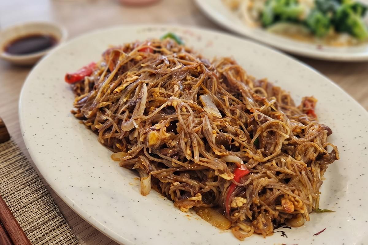 Panfried Crispy Bee Hoon signature dish from Tang Tea House served on a white oval plate with chopsticks and dipping sauce. Panfried Crispy Bee Hoon signature dish from Tang Tea House served on a white oval plate with chopsticks and dipping sauce.