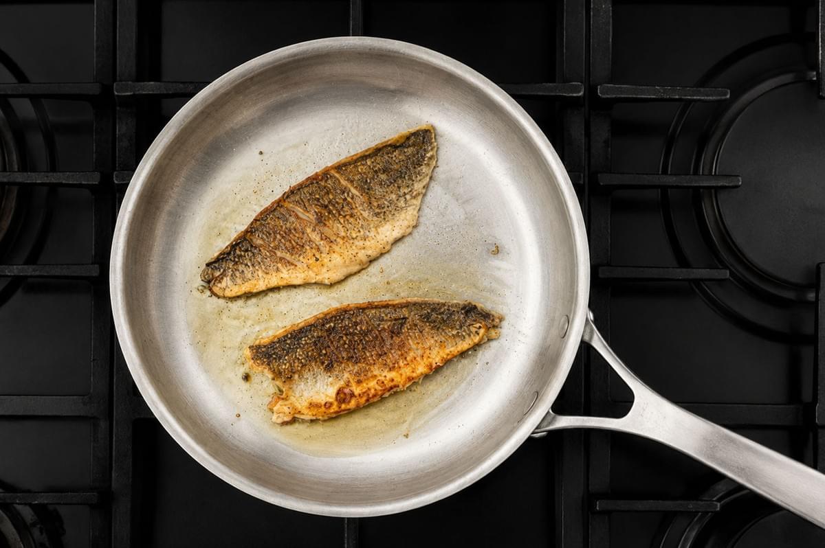 Two fish fillets searing in a stainless steel pan on a gas stovetop Two fish fillets searing in a stainless steel pan on a gas stovetop
