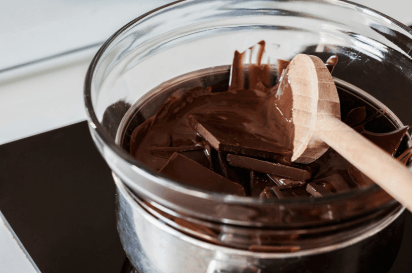 Close-up of dark chocolate chunks melting in a glass bowl set over a pot of simmering water, demonstrating the double boiler method. Close-up of dark chocolate chunks melting in a glass bowl set over a pot of simmering water, demonstrating the double boiler method.