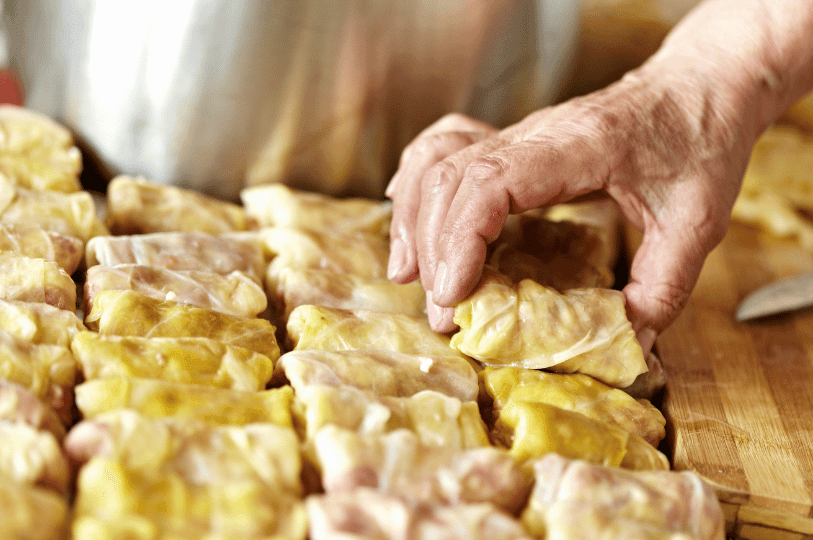 A pair of hands carefully assembling and tightly packing raw stuffed cabbage rolls together in preparation for cooking. A pair of hands carefully assembling and tightly packing raw stuffed cabbage rolls together in preparation for cooking.