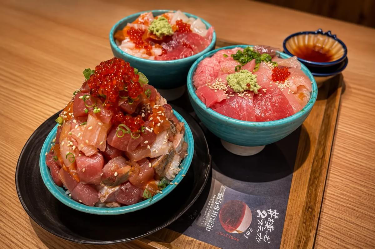 Three bowls of chirashi don topped with fresh diced sashimi, tuna, and salmon roe on a wooden table. Three bowls of chirashi don topped with fresh diced sashimi, tuna, and salmon roe on a wooden table.