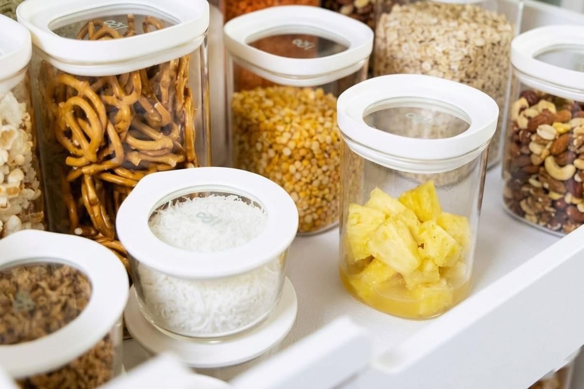 Glass storage jars with white lids filled with snacks like pretzels, nuts, and corn, alongside a jar of pineapple chunks in syrup Glass storage jars with white lids filled with snacks like pretzels, nuts, and corn, alongside a jar of pineapple chunks in syrup