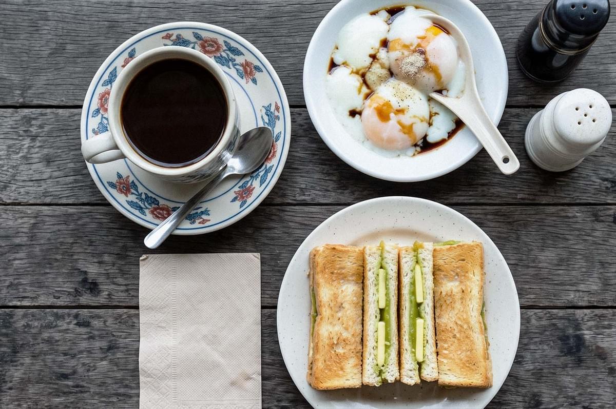Overhead view of a breakfast spread with black coffee, soft-boiled eggs drizzled with soy sauce, and toasted bread filled with slices of cucumber. Overhead view of a breakfast spread with black coffee, soft-boiled eggs drizzled with soy sauce, and toasted bread filled with slices of cucumber.