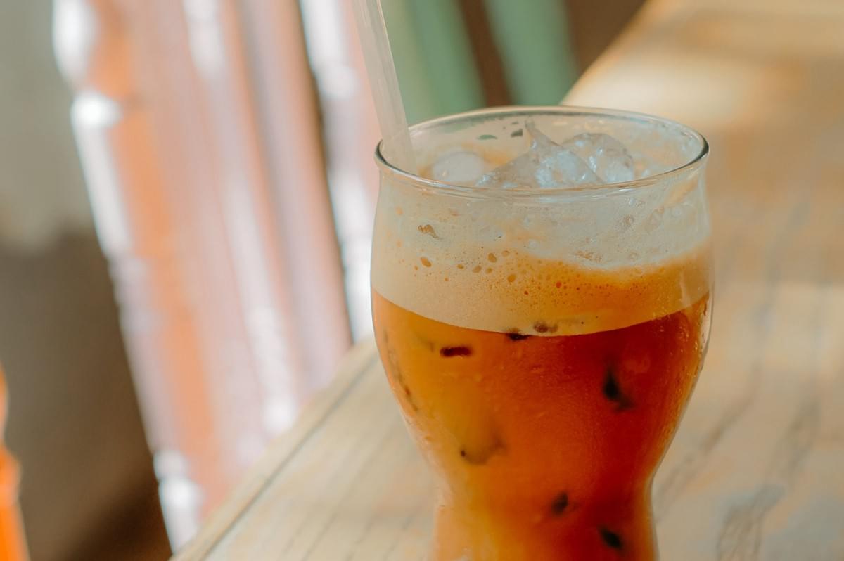 Refreshing glass of iced Thai milk tea with ice cubes and a straw. Refreshing glass of iced Thai milk tea with ice cubes and a straw.