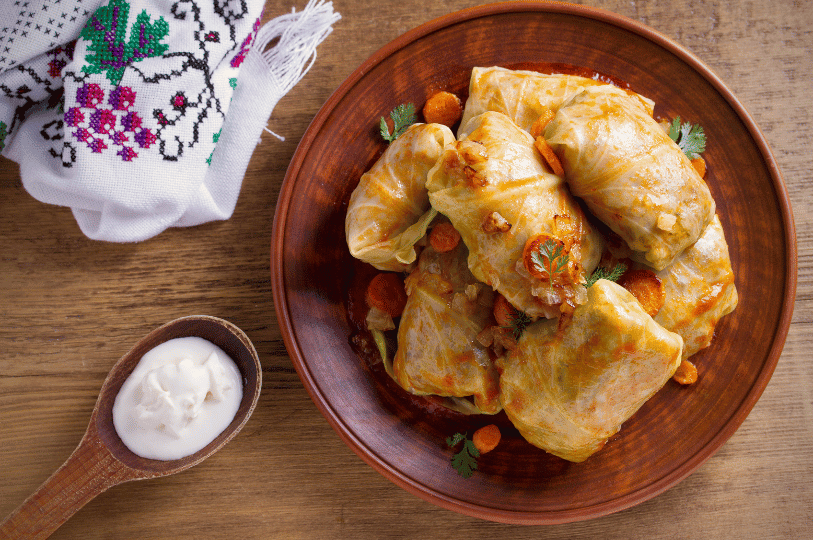 Traditional Romanian Sarmale served on a rustic brown clay plate, accompanied by a wooden spoonful of sour cream and a traditional embroidered cloth. Traditional Romanian Sarmale served on a rustic brown clay plate, accompanied by a wooden spoonful of sour cream and a traditional embroidered cloth.