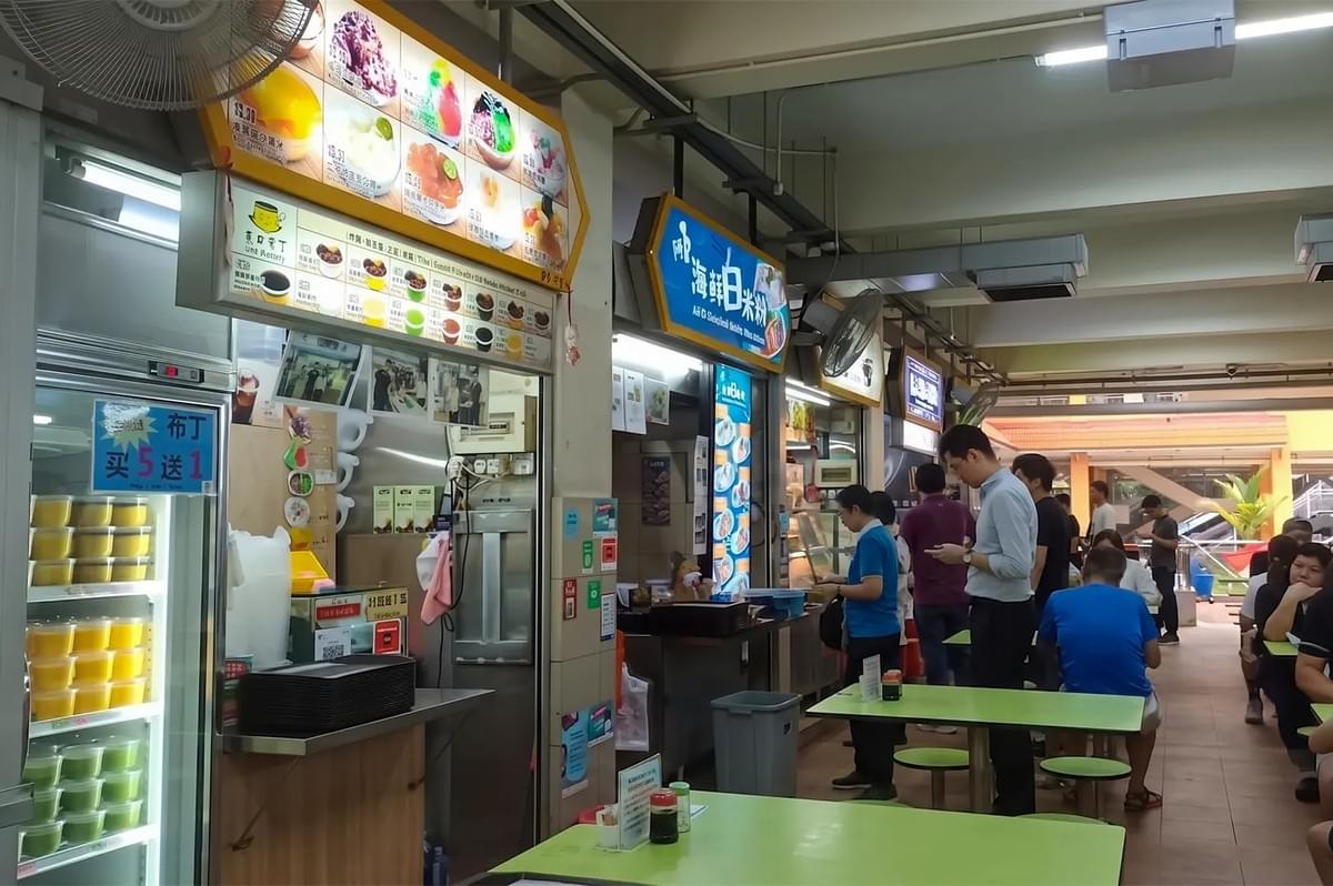 Busy Singapore hawker centre food court with customers queuing at traditional dessert and seafood stalls. Busy Singapore hawker centre food court with customers queuing at traditional dessert and seafood stalls.