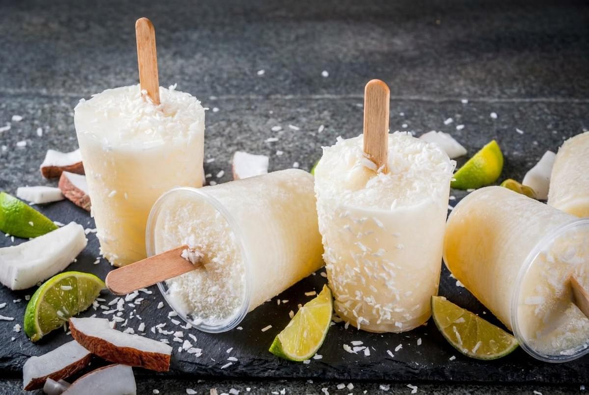 Coconut lime popsicles sprinkled with shredded coconut, surrounded by fresh lime wedges and coconut pieces. Coconut lime popsicles sprinkled with shredded coconut, surrounded by fresh lime wedges and coconut pieces.