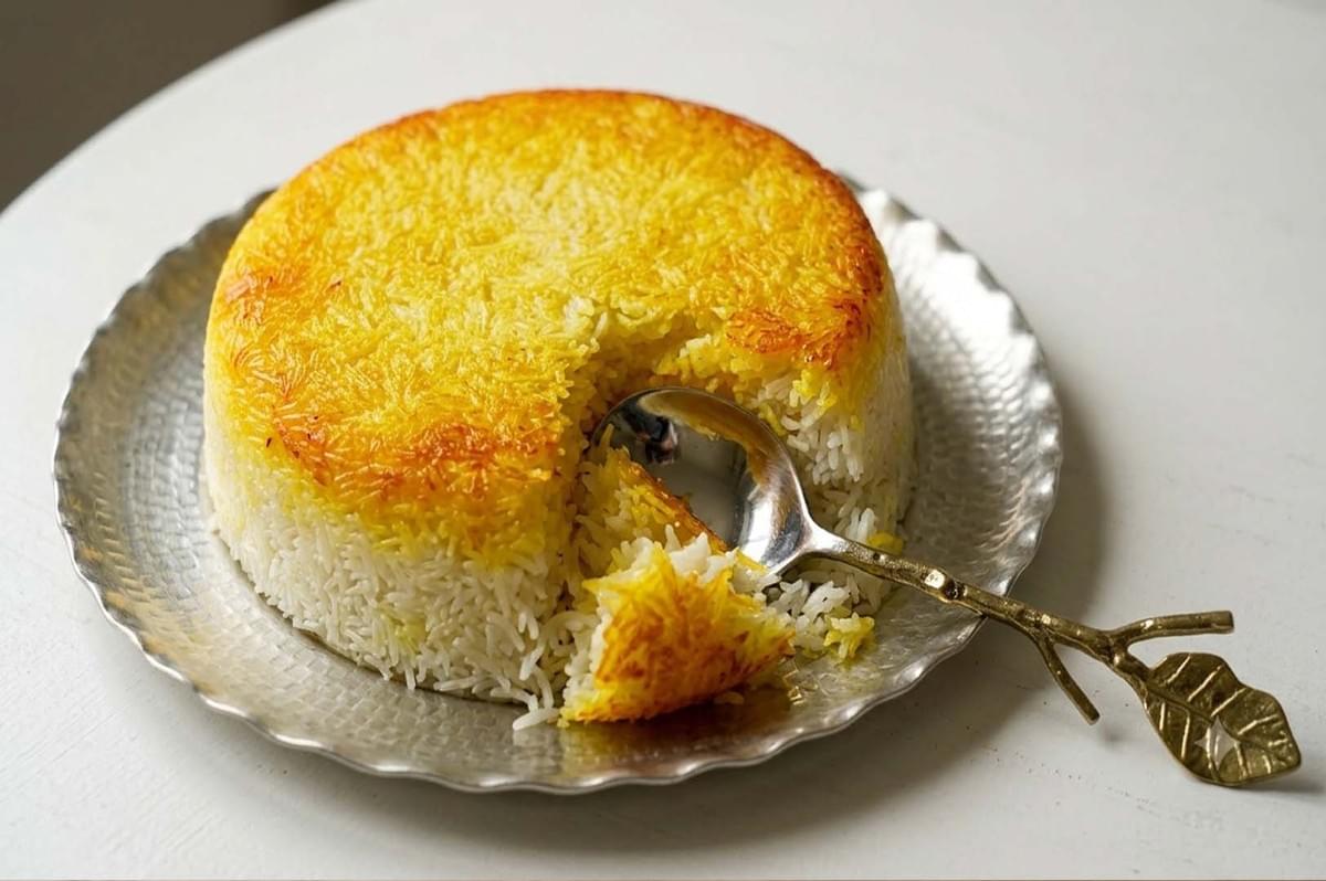 Golden crispy Tahdig rice cake on a silver plate with a spoon scoop Golden crispy Tahdig rice cake on a silver plate with a spoon scoop