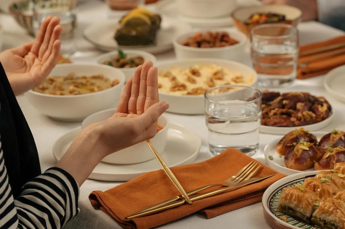 A person raising hands in quiet prayer and gratitude before a halal meal spread on a dining table. A person raising hands in quiet prayer and gratitude before a halal meal spread on a dining table.