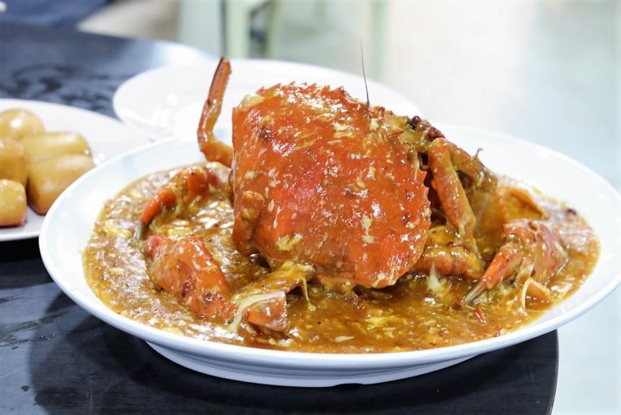 A whole cooked crab coated in a rich, savory chili egg sauce is served in a large white platter on a table. A plate of golden-brown fried mantou buns sits to the left. A whole cooked crab coated in a rich, savory chili egg sauce is served in a large white platter on a table. A plate of golden-brown fried mantou buns sits to the left.