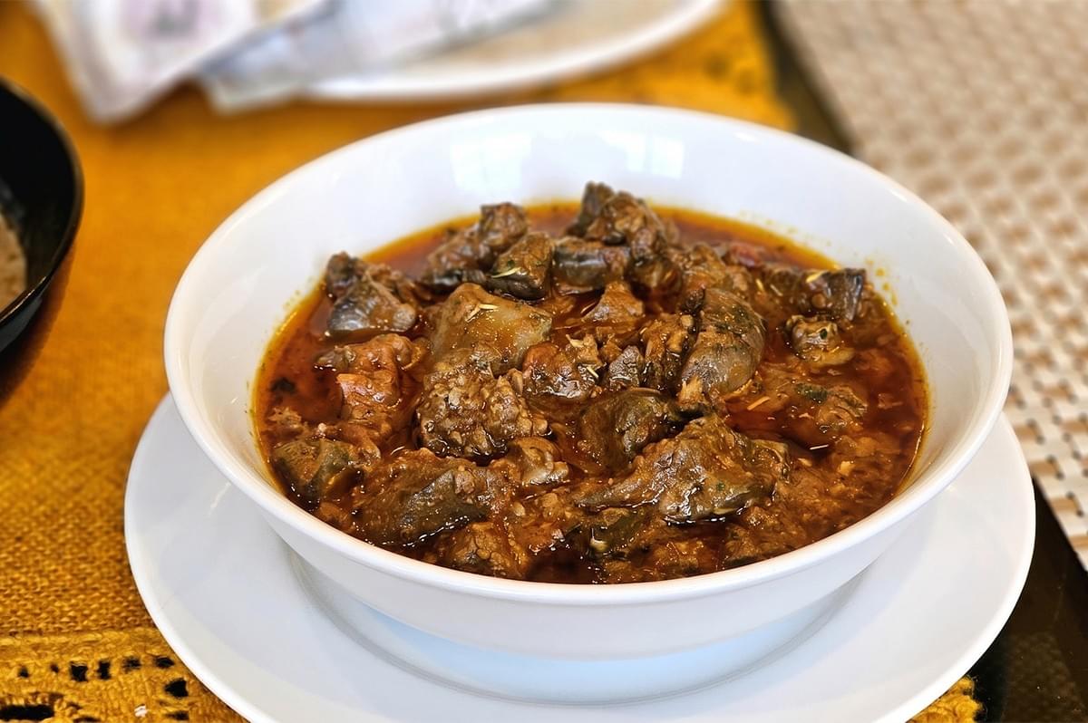 A bowl of slow-cooked beef stew in a rich savory gravy, served in a white ceramic bowl on a dining table. A bowl of slow-cooked beef stew in a rich savory gravy, served in a white ceramic bowl on a dining table.