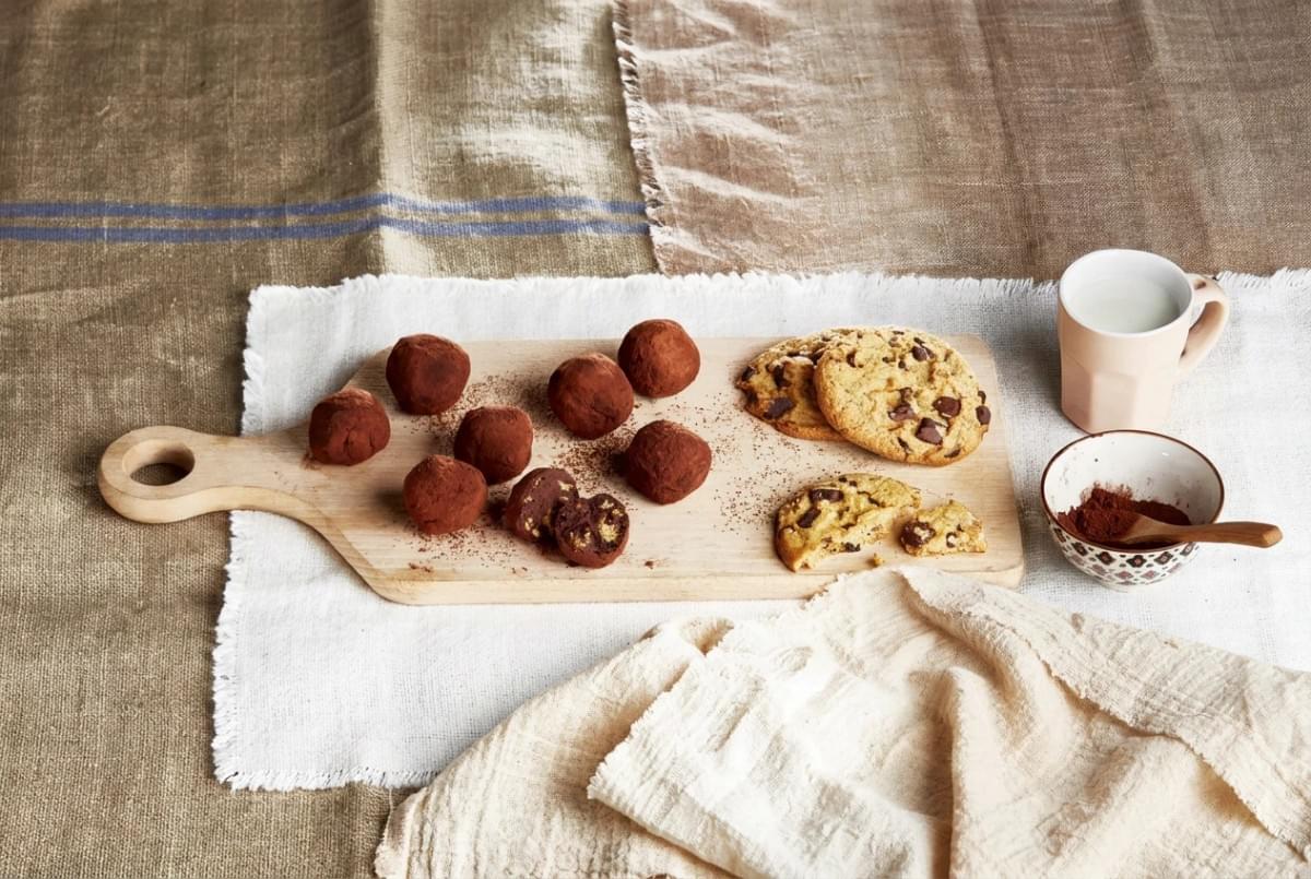 Wooden board filled with cocoa-dusted truffles, chocolate chip cookies, and a cup of milk. Wooden board filled with cocoa-dusted truffles, chocolate chip cookies, and a cup of milk.